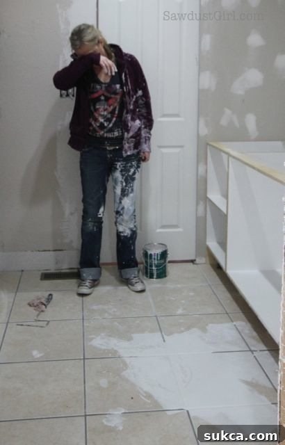 Painting blunder: A close-up view shows a hand using a paintbrush to retrieve and apply paint directly from the large spill on the floor, demonstrating resourceful salvaging.