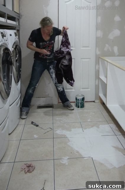 Painting blunder: A person kneels on the floor, actively painting a cabinet section, with a significant amount of white paint still visibly spilled around their workspace.