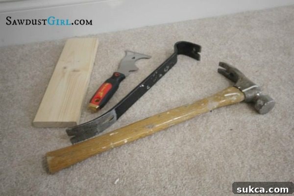 A collection of tools including a utility knife, pry bar, hammer, and painter's tool, ready for baseboard removal.