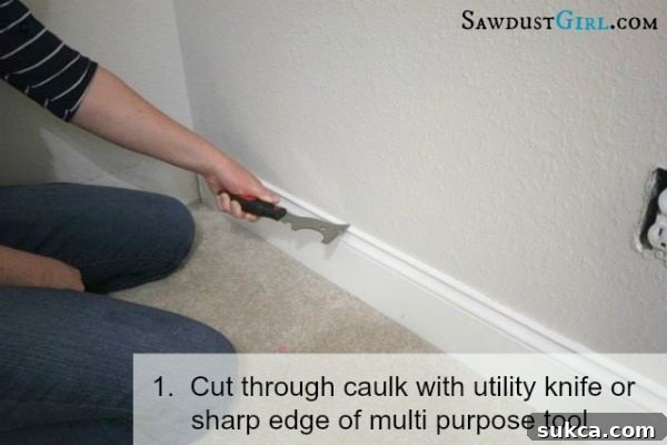Using a utility knife to score and cut through caulk where the baseboard meets the wall, preventing drywall damage.