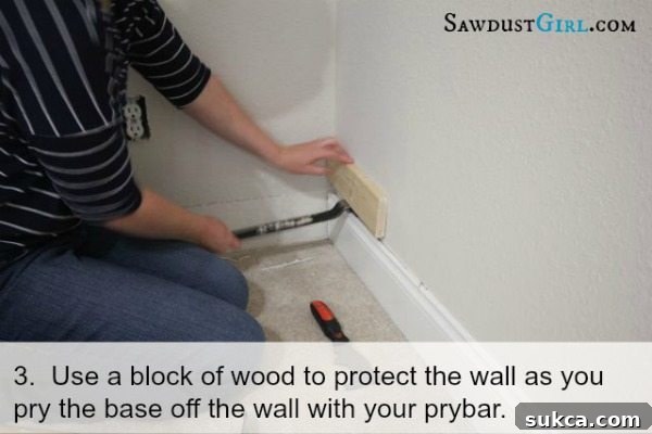 Placing a scrap wood block behind a pry bar to protect the drywall while removing baseboard trim.