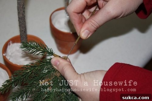Preparing Faux Pine Branches Hand stripping plastic needles off a faux pine branch to expose the wire, preparing it for insertion into a DIY topiary.