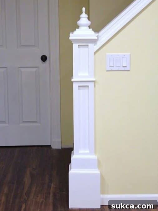 Finished DIY newel post at the end of a stair half wall, painted white with decorative trim and finial