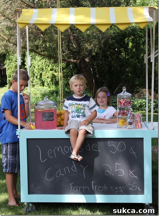 Lemonade cart with striped canopy attracting happy customers A close-up view of the lemonade stand from a customer's perspective, highlighting the cheerful atmosphere created by the spray-painted striped canopy and the happy children.