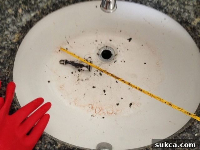 Disgusting mass of hair and black gunk extracted from a clogged drain by a Zip-it tool, held up for view.