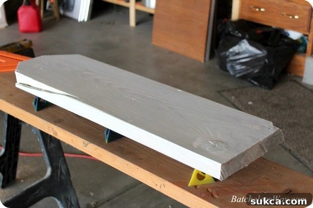 Applying a base coat of white paint to a wooden DIY headstone, demonstrating an easy, imperfect painting technique.