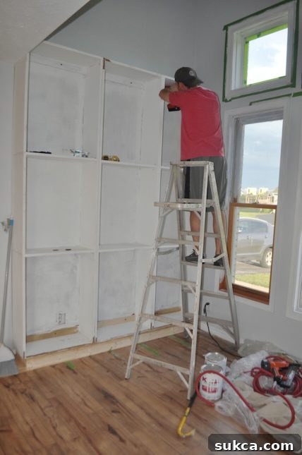 Jer attaching the built-in cabinet to the wall Husband installing built-in bookshelves to the wall securely