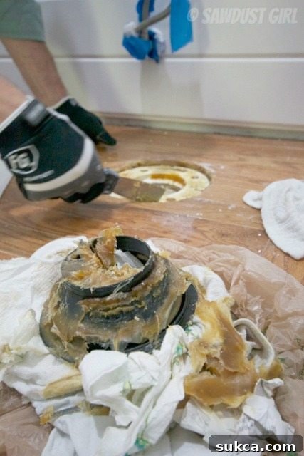 How to replace a toilet wax ring Close-up view of removing old wax ring from toilet flange during replacement.