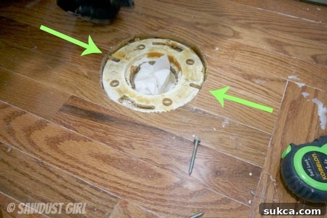 Modifying floor for toilet bolts Drilling holes in wood floor next to toilet flange to accommodate bolts.