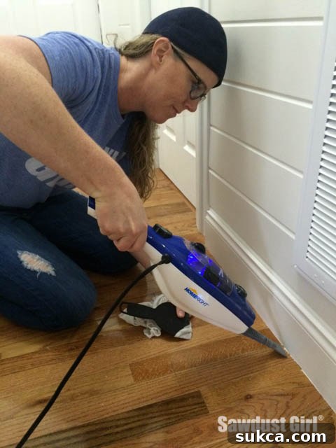 Using a plastic scraper to gently remove softened paint from a wood floor
