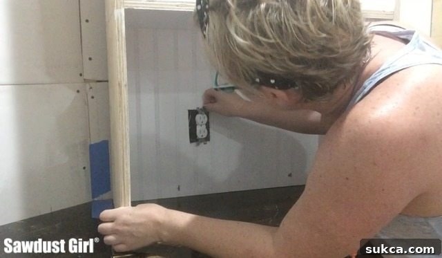 Installed lower pantry cabinets with a neatly cut-out section for an electrical outlet, showing a partially completed wall.