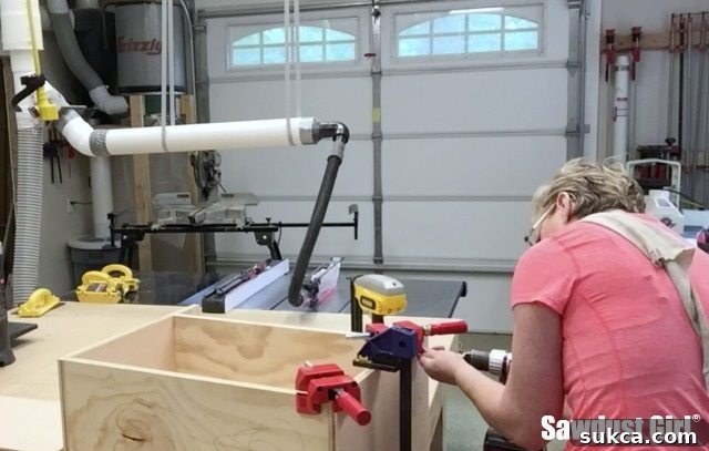 Close-up of a corner clamp holding cabinet pieces together while a screw is driven in, demonstrating efficient joinery.