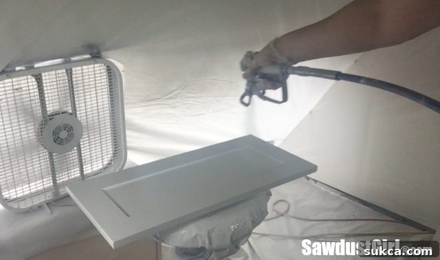 The paint sprayer in action, applying an even coat to a cabinet door, demonstrating precise technique for a smooth finish.