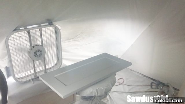 The DIY swivel paint stand in full operation, effortlessly rotating a cabinet door for even spray paint application.