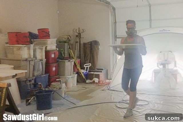 A freshly painted cabinet door being carefully moved from the spray booth to a simple yet effective DIY drying rack, ensuring proper air circulation.
