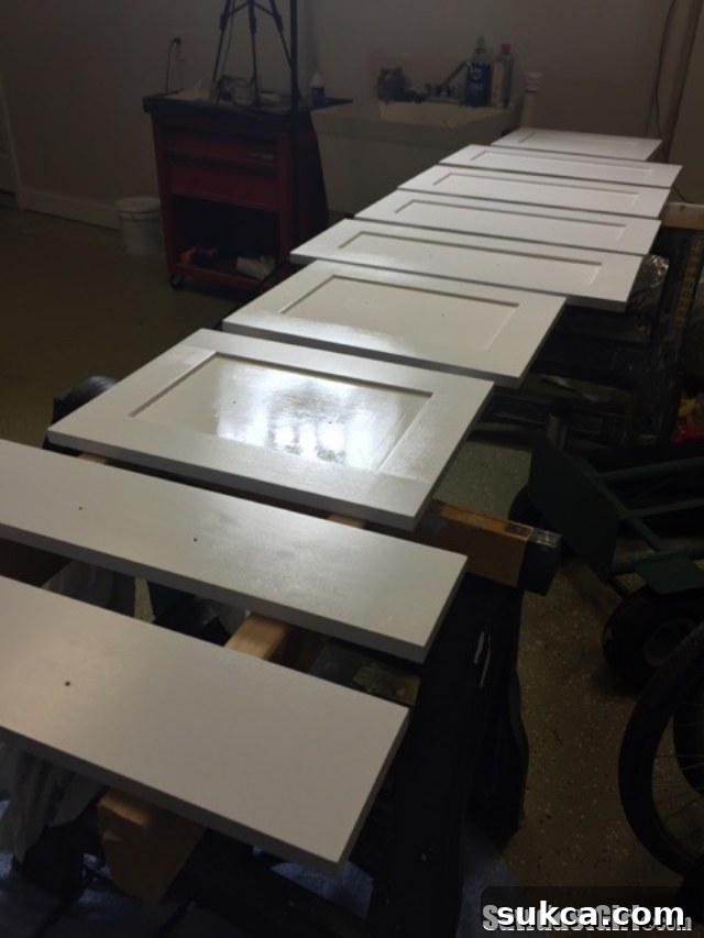 A series of newly spray-painted cabinet doors resting on a DIY drying rack made from 2x4s and sawhorses, allowing for optimal air circulation.