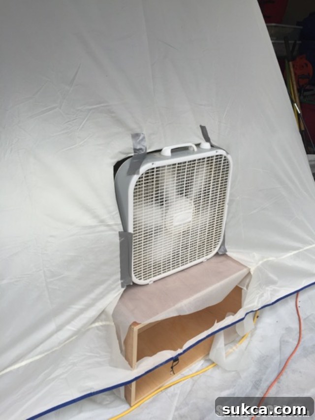 A modified spray shelter with a square cut-out in the back to install a box fan, enhancing ventilation and overspray extraction.