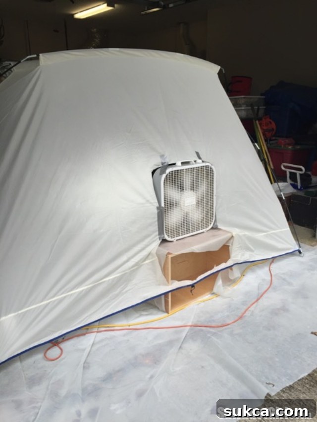 Close-up of a box fan installed in the rear opening of a spray shelter, specifically designed to pull overspray out of the booth.