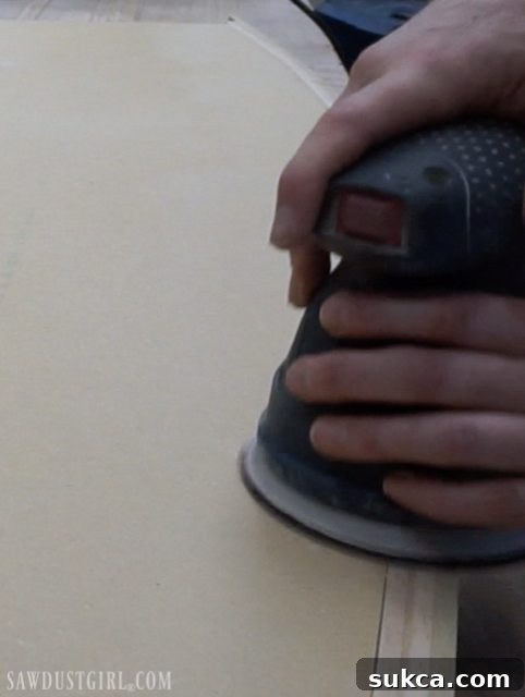 Smoothing out the top surface of a DIY desktop with an orbital sander, ensuring flush joints