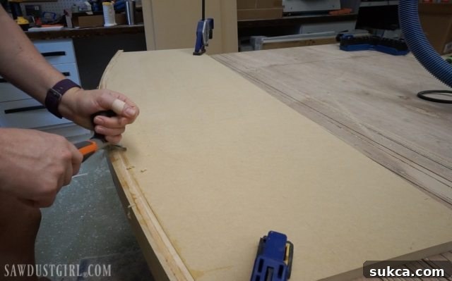 Using a wood scraper to efficiently remove excess dried glue from the desk surface before sanding