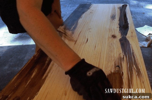 Applying dark brown Briwax to bare wood with a soft cloth, following the grain for an even, rich stain.