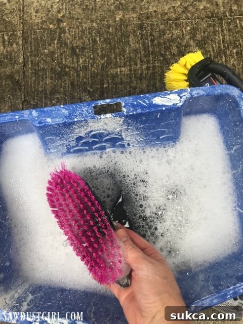 Essential cleaning supplies for garage doors: scrub brush, bucket with soapy water, and foaming bathroom cleaner with bleach