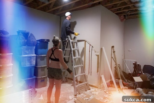 Woman in shorts and sports bra, working on basement demolition with helper, highlighting the physical demands of renovation