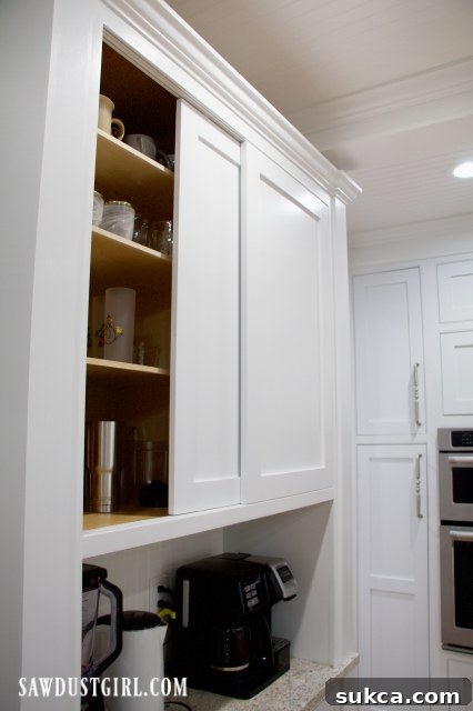 Sleek sliding doors elegantly concealing cups and glasses in a modern coffee bar cabinet, showcasing functional kitchen design.