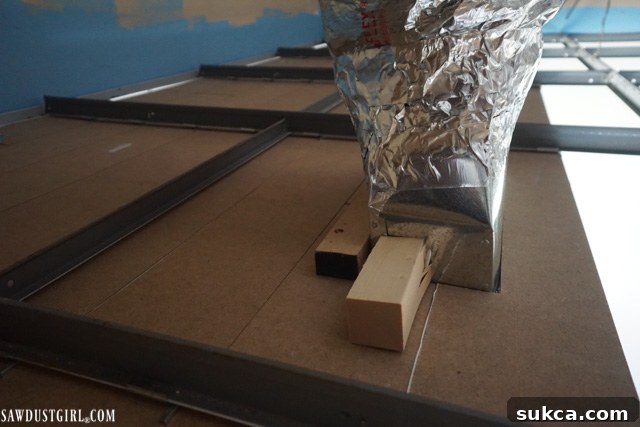 A piece of scrap wood used as a backing for screws to secure the vent cover to thin ceiling planks, ensuring a strong hold.