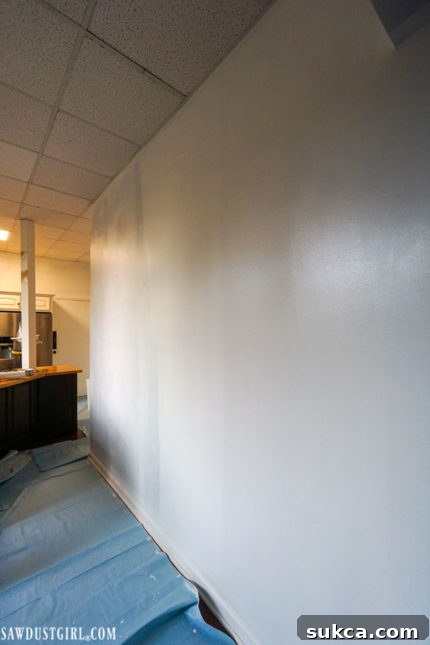 White Paint Over Dark Walls The striking visual contrast of the first coat of bright white paint applied over the dark brown kitchen wall, showing an immediate and dramatic transformation.
