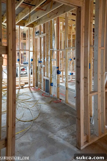 The framed laundry room with visible plumbing and electrical connections, showing preparations for future appliances and utility hook-ups.