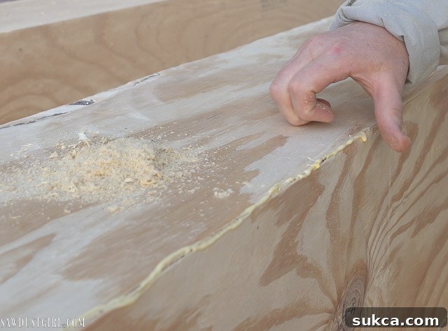 Sawdust being pressed into a crack in the faux beam after applying glue, to fill and distress.