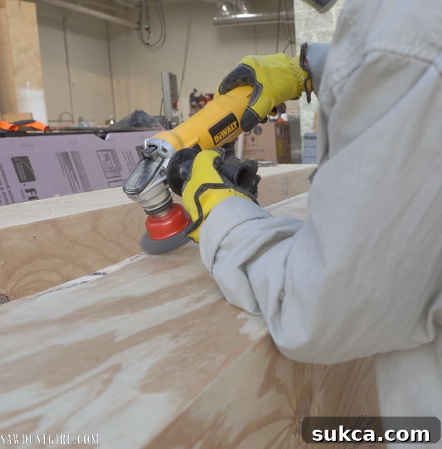 A person using a grinder with a wire sanding wheel to aggressively distress the wood beam.