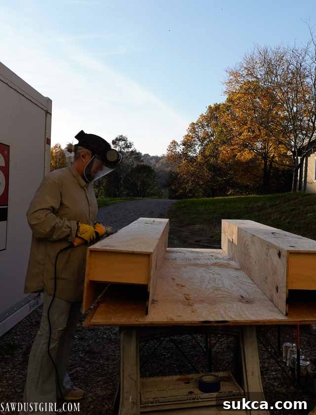 A person wearing a full face respirator and protective gear while distressing wood.