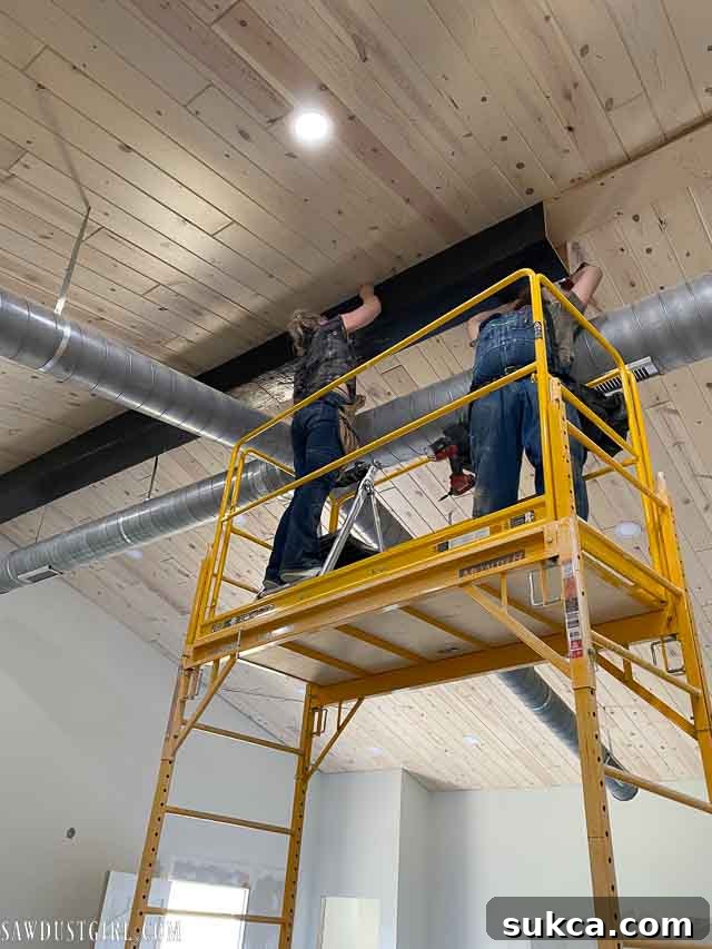 Working around HVAC ducting during faux beam installation, showing awkward body positioning.