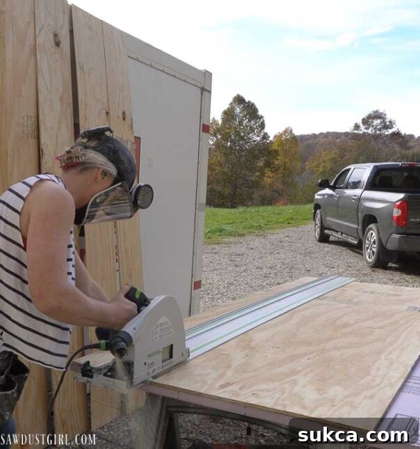 A person using a track saw to cut a large sheet of plywood into strips.