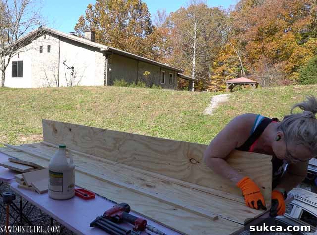 A person holding together large plywood pieces to form a faux beam section during assembly.