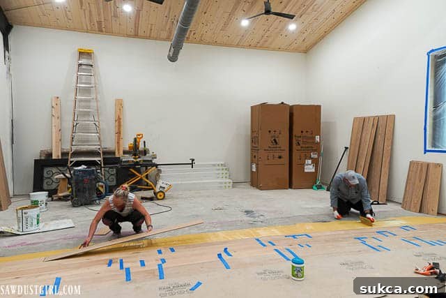 Renovation progress on the living room floor, showing initial rows of engineered wood planks being glued down.