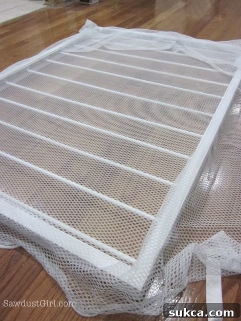 Stretching and stapling the netting onto the drying rack frame using hardboard strips.